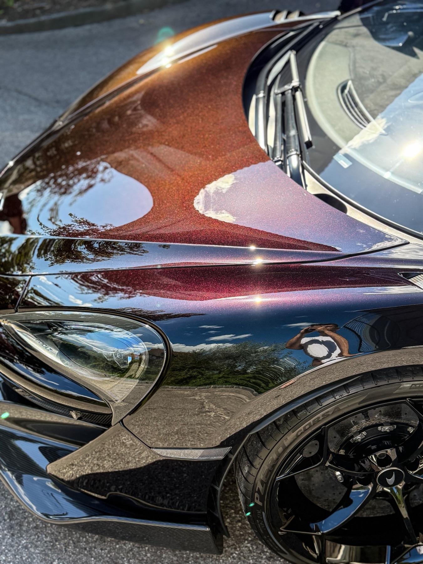 Dunkler Lack auf der Motorhaube, darin spiegeln sich Bäume und Himmel