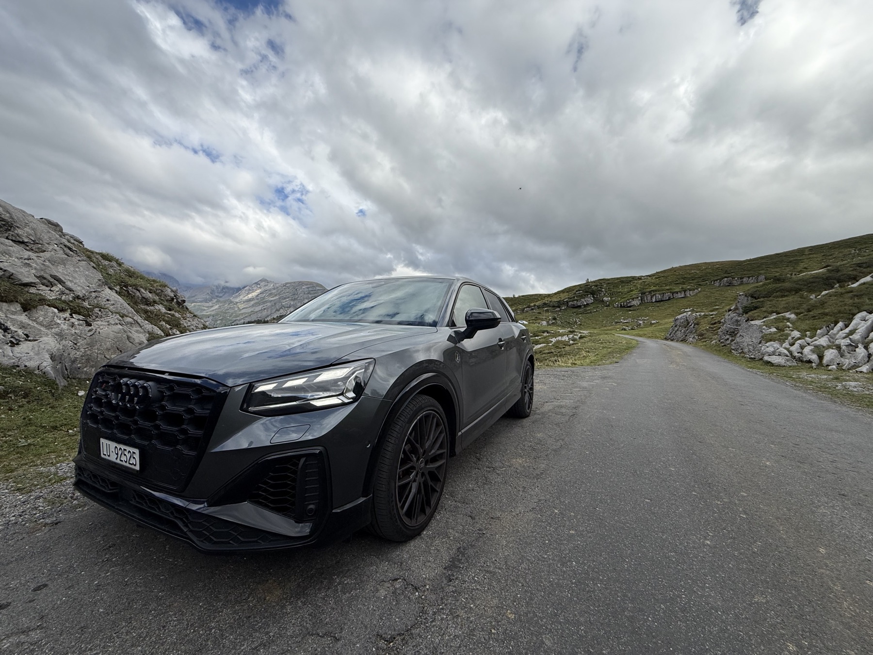 Dunkler Audi auf einer Bergstrasse unter Wolken